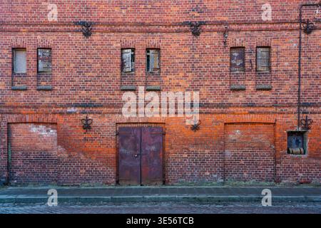 Alte rote Backsteinfassade mit rostiger Tür und verdeckten Fenstern, urbaner Dekorationsszene Stockfoto