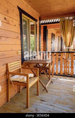 Sonnige Holzterrasse mit Tisch und Stühlen in gemütlicher Kabine außen Stockfoto