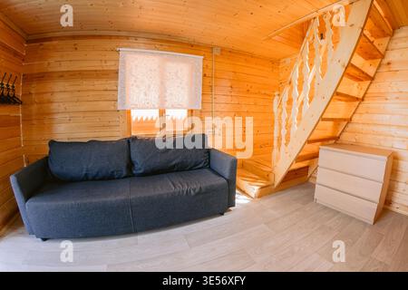 Gemütliches hölzernes Wohnzimmer mit Sofa, Treppe und warmer natürlicher Inneneinrichtung im Kabinenstil, Gastfamilie Stockfoto