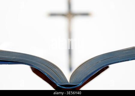 Öffnen Sie die Bibel auf einem Rednerpult mit einem schwarzen Kruzifix, das im Hintergrund sichtbar ist. Stockfoto