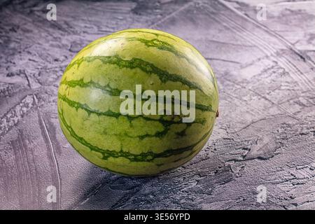 Nahaufnahme einer ganzen, gestreiften grünen Wassermelone auf einer strukturierten grauen Beton- oder Schieferoberfläche. Einfache, minimalistische Komposition mit Kopierraum. Konzept für Stockfoto
