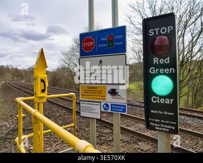 Derbyshire, UK - 26. Mär 2026: Fußgänger-Schiene Überführung mit grünem Freigabesignal und Sicherheitsschildern neben den Bahngleisen in Derbyshire UK unter einem bewölkten Frühlingshimmel Stockfoto