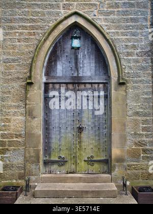 Yorkshire, UK - 14. Mär 2026: Verwitterte hölzerne Kirchentür in einem spitzen Steinbogen der St Mary the Virgin Church in Ramsgill Yorkshire UK mit einer zeitlosen rustikalen Atmosphäre Stockfoto