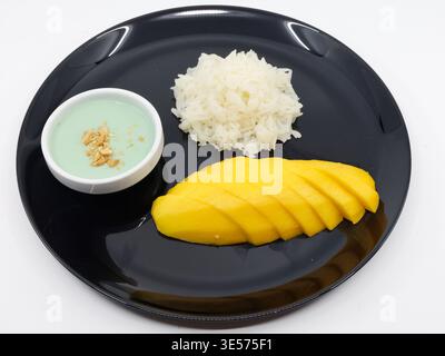 Asiatische Küche. Klassisches thailändisches Mango-Reisdessert mit Kokosnusscreme-Sauce auf schwarzem Teller. Stockfoto