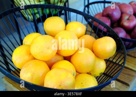 Schüssel mit frischen Orangen und roten Äpfeln in schwarzen Drahtkörben auf Holzoberfläche. Sopot. Polen. Stockfoto