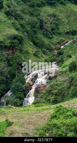 Ein kleiner, aber schöner Wasserfall, der sanft über Felsen stürzt, umgeben von üppigem Grün, schafft eine friedliche und erfrischende natürliche Szene. Stockfoto