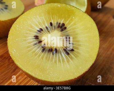 Nahaufnahme eines Makrofotos einer frischen, goldenen Kiwi-Frucht, die im halben Querschnitt geschnitten ist und lebendiges gelb-grünes Fruchtfleisch mit weißem Kern und zeigt Stockfoto
