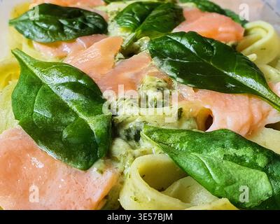 Nahaufnahme eines Makrofotos eines frischen italienischen Nudelgerichts mit Tagliatelle-Nudeln, belegt mit rosa Räucherlachs und leuchtendem grünem Basilikum Stockfoto