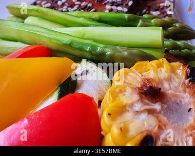 Makroaufnahme mit verschiedenen gegrillten Gemüsesorten, einschließlich grüner Spargelstangen, roter und gelber Paprikascheiben, Zucchini-Runden und Mais Stockfoto