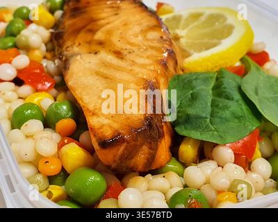 Nahaufnahme eines gegrillten Lachsfilet mit karamelisierter Glasur und sichtbaren Grillspuren, serviert über Perlmutt-Couscous mit bunten Gemüse Stockfoto