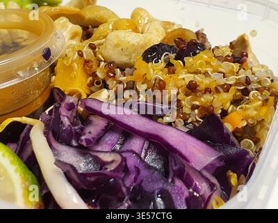 Ein Nahfoto einer bunten gesunden Kornschale, serviert in einem durchsichtigen Plastikbehälter zum Mitnehmen. Das Gericht besteht aus einer Mischung aus weißem und rotem Quinoa Stockfoto
