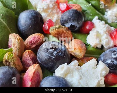 Makrofoto von einem frischen Salat oder einem gesunden Gericht mit dicken dunklen Heidelbeeren, schalen Pistazien-Nüssen mit sichtbarem violett und grün Stockfoto