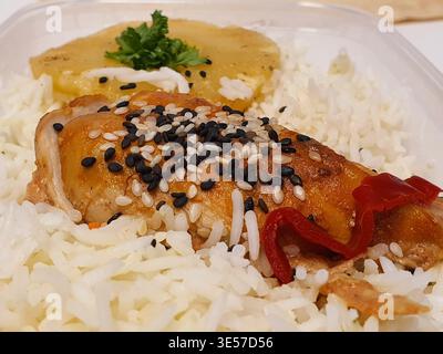 Nahaufnahme einer zubereiteten Mahlzeit, die in einem durchsichtigen Plastikbehälter serviert wird, mit einem Bett aus flauschigem weißem Langkornreis und goldbraunem Reis Stockfoto