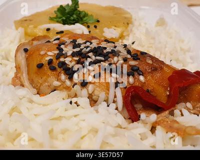 Nahaufnahme einer zubereiteten Mahlzeit mit goldbraun gebratenem Huhn, belegt mit schwarz-weißen Sesamsamen, serviert auf einem flauschigen Bett Stockfoto