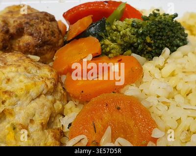 Nahaufnahme eines Makrofotos einer zubereiteten Mahlzeit mit weißem Reis, in Scheiben geschnittenen OrangenKarotten, grünen Brokkoli-Röschen und roten Paprika-Stücken. Die Stockfoto