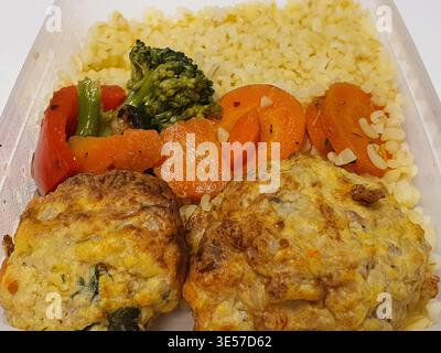 Eine Nahaufnahme einer zubereiteten Mahlzeit in einem rechteckigen Plastikbehälter mit zwei goldbraunen Fleischpasteten im Vordergrund, begleitet von Stockfoto