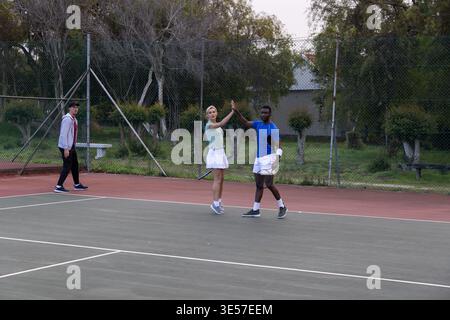 Diverse Tennispartner spielen im Netz auf dem Platz im Freien, tragen Sportbekleidung und halten Schläger Stockfoto