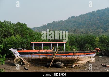 Ein altes Fischerboot liegt verlassen an der matschigen Küste, umgeben von üppigem Grün und Hügeln in Indien. Ein ruhiger und doch rustikaler Reisemoment in sich Stockfoto