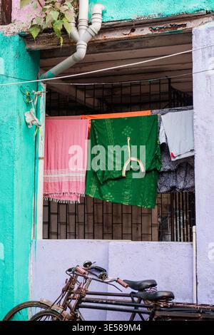 Eine lebhafte Straßenszene in Indien zeigt farbenfrohe Wäsche, die an einer Linie über zwei verwitterten Fahrrädern hängt, vor hell bemalten Wänden, Capturin Stockfoto