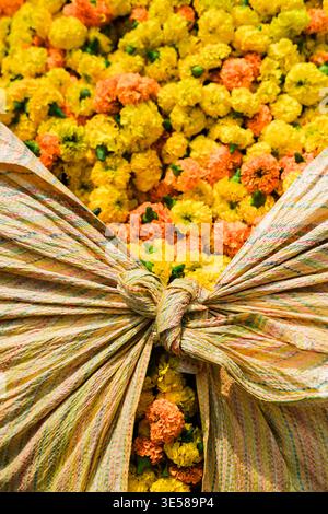 Nahaufnahme von leuchtenden gelben und orangen Ringelblumen, die in farbenfrohe Stoffe gewickelt sind. Dieses traditionelle indische Blumenarrangement symbolisiert die Feier A Stockfoto