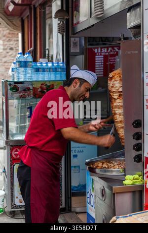 Ein türkischer Kebab-Koch in roten Uniformen schneidet Fleisch von einer rotierenden Dönerspieße an einem Street Food-Stand in Istanbul, Türkei Stockfoto
