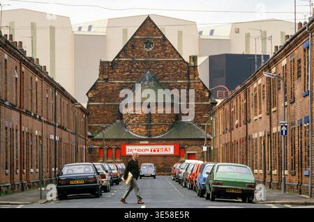Barrow-in-Furness 1980s UK. Die riesige Devonshire Dock Hall (DDH), „Maggie's Shed“ (benannt nach Margaret Thatcher) bei Vickers Shipbuilding and Engineering, Ltd (VSEL), dominiert die Skyline der Schiffbaustädte. Traditionelles Reihengehäuse der Arbeiterklasse. Cumbria, England um 1985. HOMER SYKES Stockfoto