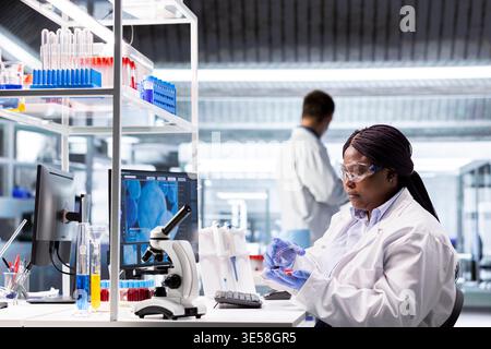 Wissenschaftlerin studiert Petrischale im modernen Labor mit Pathologieuntersuchung, Molekularanalyse und biochemischer Forschung. Innovation in Diagnostik und Biotechnologie. Stockfoto