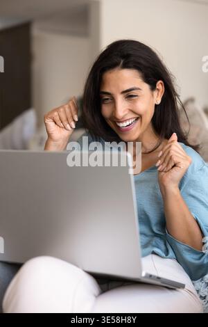Fröhliche Latina-Frau, die unglaubliche Nachrichten auf dem Laptop liest Stockfoto