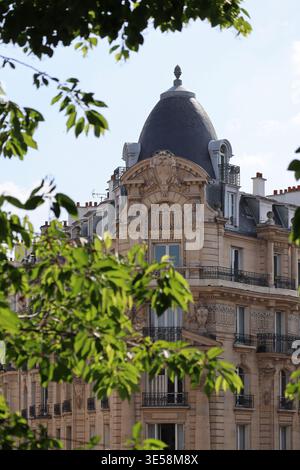 Paris, Frankreich - 7. Mai 2022: Verziertes Gebäude im Haussmann-Stil mit Kuppeldach und reicher dekorativer Fassade, eingerahmt von grünen Blättern im Stadtteil Bastille Stockfoto