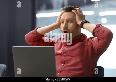 Der Mann sieht schockiert aus, wenn er während der Arbeitszeit im Büro einen Laptop verwendet Stockfoto