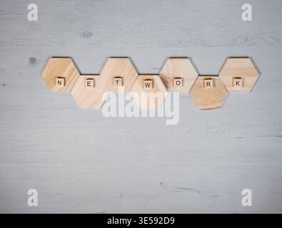Hölzerne sechseckige Fliesen und Buchstabenblöcke Rechtschreibnetzwerk auf hellgrauem Holzhintergrund, symbolisieren Verbindung, Zusammenarbeit, Teamarbeit und digitale Kommunikation Stockfoto