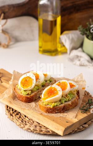 Zwei Scheiben knuspriger Sauerteig, belegt mit Avocadopüree und marmelierten mittelgekochten Eiern. Die Szene bietet helles natürliches Licht auf einem rustikalen Holz Stockfoto