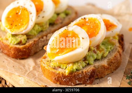 Zwei Scheiben knuspriger Sauerteig, belegt mit Avocadopüree und marmelierten weichen gekochten Eiern. Warme, natürliche Beleuchtung hebt die cremige Dotterstruktur und cra hervor Stockfoto