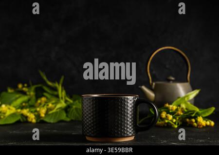 Tasse und Teekanne heißer Lindentee mit Blumen auf schwarzem Hintergrund Stockfoto