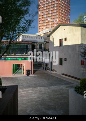 Leerer gepflasterter Innenhof mit einer Wendeltreppe aus Metall und renovierten Gebäuden, im Kontrast zu den hoch aufragenden modernen Wohnhochhäusern im hinteren Bereich Stockfoto