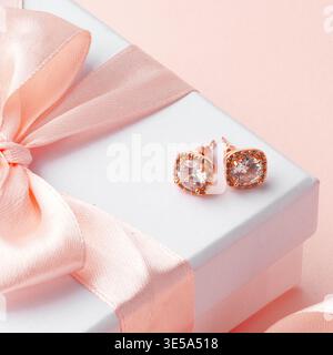 Rosafarbene Ohrringe auf einer Geschenkbox mit Schleife und Band auf hellem Hintergrund Stockfoto