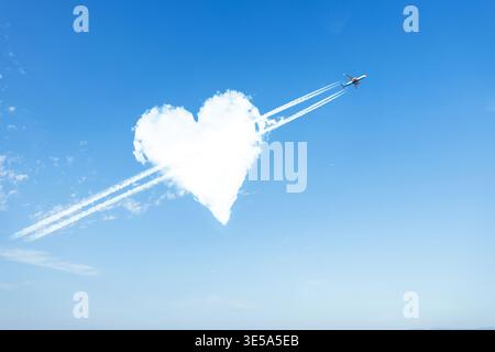 Ein kreatives Konzept mit einer flauschigen, weißen, herzförmigen Wolke in einem hellblauen Himmel, durchbohrt von einem Jet-Flugzeug, das lange Dampfspuren hinterlässt. Ein perfektes Ich Stockfoto
