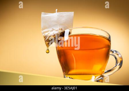 Glasbecher Tee mit tropfender Teebeutel auf gelbem Hintergrund Stockfoto