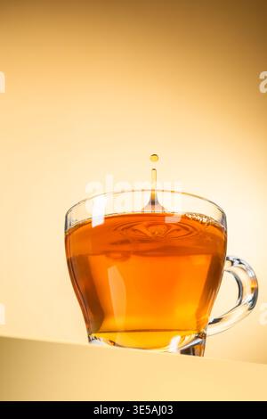Glasbecher Tee mit tropfendem Tropfen auf gelbem Hintergrund Stockfoto