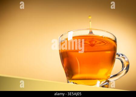 Glasbecher Tee mit tropfendem Tropfen auf gelbem Hintergrund Stockfoto