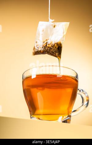 Glasbecher Tee mit tropfender Teebeutel auf gelbem Hintergrund Stockfoto
