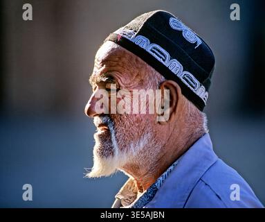 Ein älterer Mann spaziert in Chiwa, Usbekistan, mit traditioneller Kleidung. Sein Gesicht zeigt Zeichen von Alter und Erfahrung im sonnigen Licht. Stockfoto