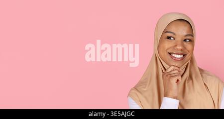 Eine junge schwarze Muslimbrau im Hijab lächelt und blickt nachdenklich zur Seite Stockfoto