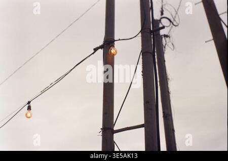 Glühlampen an Strommasten vor grauem Himmel Stockfoto