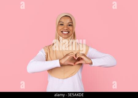 Junge schwarze muslimische Frau im Hijab, die Herzform mit Händen bildet Stockfoto