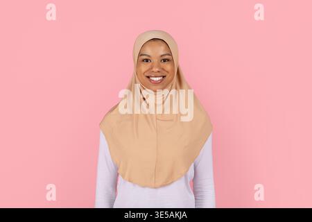 Junge schwarze muslimische Frau in beigem Hijab lächelt selbstbewusst vor der Kamera Stockfoto