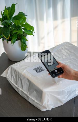 Person scannt QR-Code auf dem Paket mit Smartphone-Kamera, um die Zustellung zu Hause zu verfolgen. Mobile App mit kontaktloser Technologie und digitalem Servicekonzept. Stockfoto