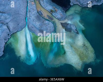 Blick von oben auf die abstrakte Winterlandschaft mit eisiger Textur, gefrorener Erde und lebendigem türkisfarbenem Seenwasser fließt in die abgelegene Wildnis Stockfoto