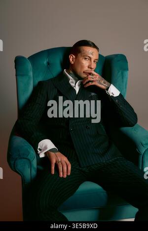 Ein junger Mann mit auffälligen Lounges in einem stilvollen blauen Stuhl, der Mode zeigt. Stockfoto