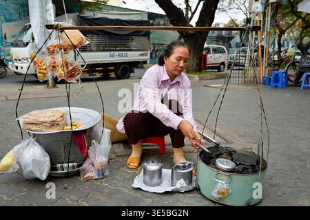 Ein Straßenverkäufer in Ho-Chi-Minh-Stadt kocht Essen auf dem Bürgersteig. Sie richtet ihren Stand mit Zutaten und Kochgeschirr auf. Stockfoto